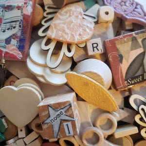 May include: A collection of assorted craft supplies including wooden hearts, a spool, a Scrabble tile with the letter R, a small block with a star and the word home, a gold-painted oval piece, and various decorative wooden shapes and cutouts.