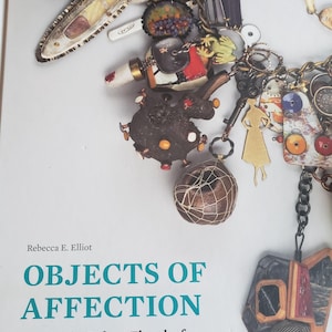 May include: A book cover titled Objects of Affection: Jewelry by Robert Ebendorf from the Porter Price Collection. The cover features a photograph of a charm necklace with various mixed-media pendants, including a gold figure, keys, and beads.