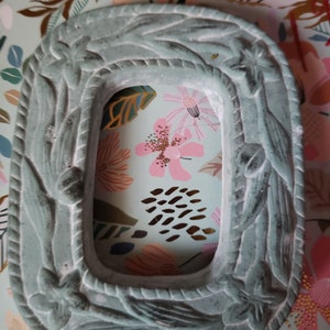 May include: A light blue, decorative, ceramic frame with a rope-like design around the edge. The frame has a rectangular opening in the center.
