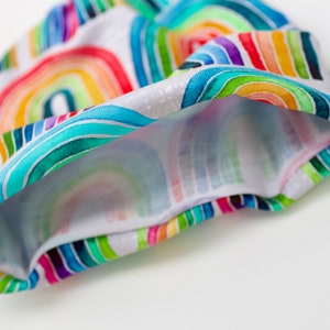 May include: A white fabric headband with a colorful rainbow pattern. The headband is folded in half, showing the inside of the fabric.