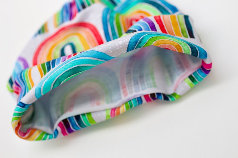 May include: A white fabric headband with a colorful rainbow pattern. The headband is folded in half, showing the inside of the fabric.