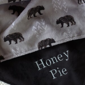May include: A soft, grey and black fleece blanket with a bear print on one side and the name "Honey Pie" embroidered on the other side.