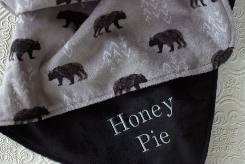 May include: A soft, grey and black fleece blanket with a bear print on one side and the name "Honey Pie" embroidered on the other side.