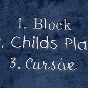 May include: A blue fabric with white embroidered text that reads "1. Block", "2. Childs Play", and "3. Cursive".