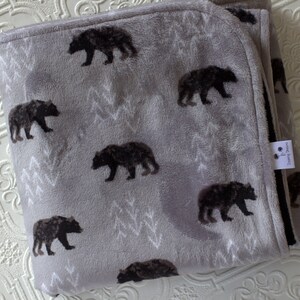 May include: A grey fleece blanket with a black bear print. The blanket has a white border and a small tag with the text "Dreaming Dreams".