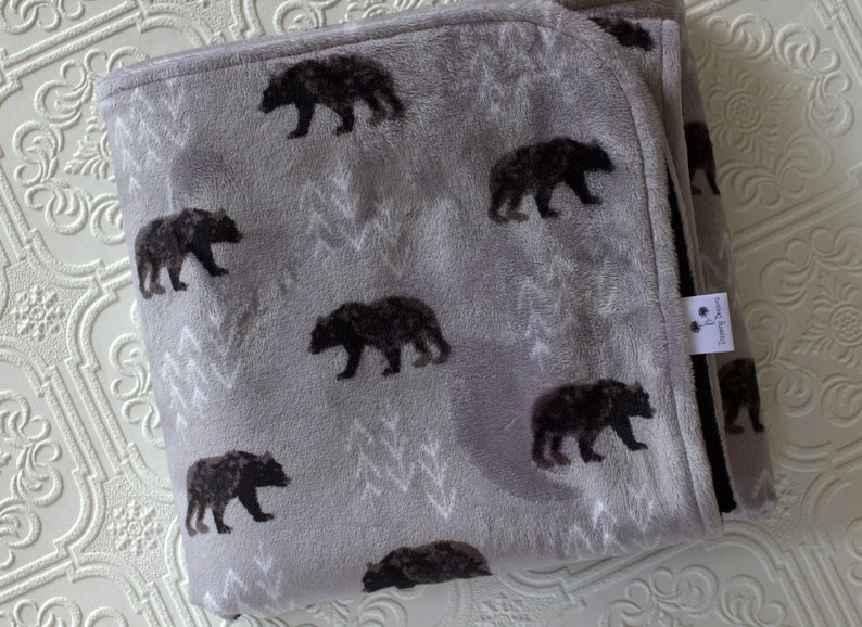 May include: A grey fleece blanket with a black bear print. The blanket has a white border and a small tag with the text "Dreaming Dreams".