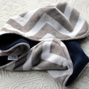 May include: A gray and white chevron patterned hooded baby blanket with a navy blue fleece lining. The blanket has a small tag that says "Sleepy Dreams".