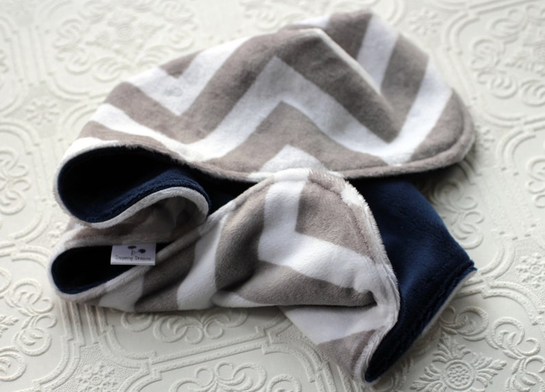 May include: A gray and white chevron patterned hooded baby blanket with a navy blue fleece lining. The blanket has a small tag that says "Sleepy Dreams".