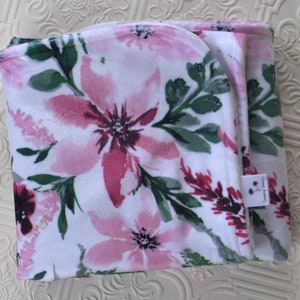 May include: A white baby blanket with a pink and green floral print. The blanket is folded in half and has a small tag that says "Sweet Dreams".