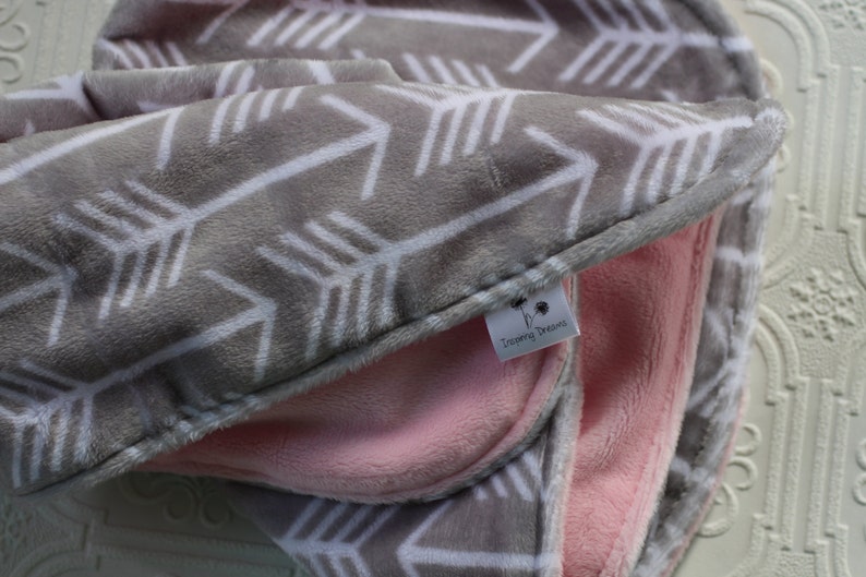 May include: A gray and white arrow print baby blanket with a pink fleece lining. The blanket has a small tag that says "Twirling Dreams".