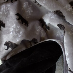 May include: A soft, grey and black fleece blanket with a repeating pattern of bears and trees. The blanket is folded in half, showing both sides.