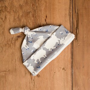 May include: Gray and white baby hat with a knot on top. The hat has a pattern of white goats on a gray background.