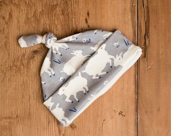 May include: Gray and white baby hat with a knot on top. The hat has a pattern of white goats on a gray background.