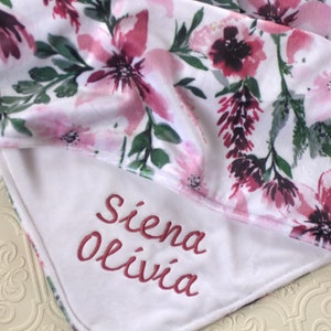 May include: White baby blanket with a pink floral print and the names "Siena Olivia" embroidered in pink on the white side.
