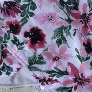May include: A white fabric with a pink and burgundy floral pattern. The fabric has a soft, fuzzy texture.