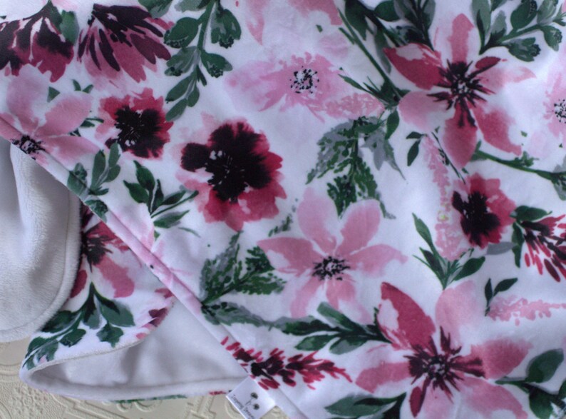 May include: A white fabric with a pink and burgundy floral pattern. The fabric has a soft, fuzzy texture.