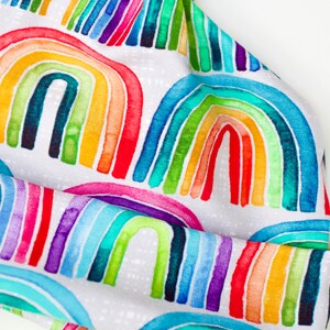 May include: A white beanie hat with a colorful rainbow pattern. The rainbow is made up of watercolor-like stripes in shades of red, orange, yellow, green, blue, indigo, and violet.