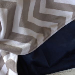 May include: A chevron patterned throw blanket in beige and white with a dark blue backing.