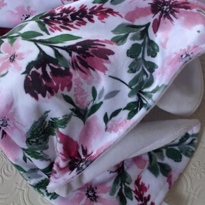 May include: A white blanket with a floral pattern in shades of pink and green. The blanket is folded in half and the fabric is soft and plush.