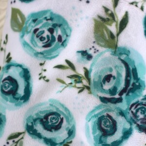 May include: White plush blanket with a teal floral pattern. The blanket features a repeating pattern of teal roses with green leaves.