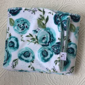 May include: A white and teal floral print blanket with a soft, plush texture. The blanket is folded in half and has a small tag that says "Sleeping Dreams".