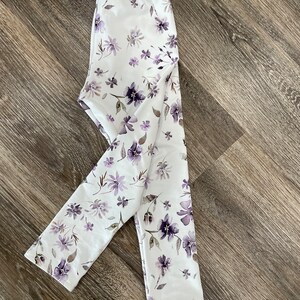 May include: White leggings with a purple floral print. The leggings are made of a soft, stretchy fabric and are perfect for everyday wear.