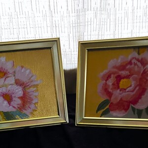 May include: Two framed paintings with gold frames. The paintings feature pink flowers on a gold background.