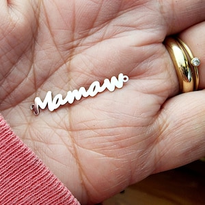 May include: A silver charm with the word "Mamaw" written in a cursive font.