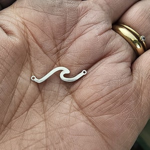 May include: Silver wave charm with two jump rings. The charm is in the shape of a wave with a smooth, rounded surface.