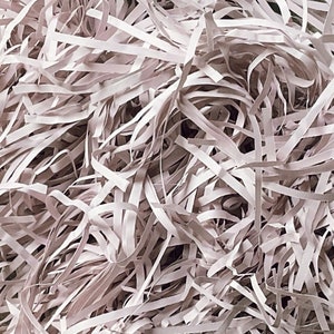 Op de afbeelding: Een close-up van een stapel gescheurd papier. Het papier is lichtgrijs van kleur en is in lange, dunne stroken.
