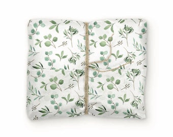 May include: A square package wrapped in white paper featuring a repeating pattern of green eucalyptus leaves and thin branches. The package is secured with a single length of thin, natural brown twine tied in a simple knot across the center.