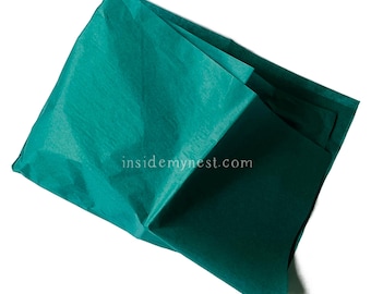 May include: A folded teal tissue paper with a textured surface. The tissue paper is a deep shade of teal and is layered, with visible folds and shadows. The website address "insidemynest.com" is visible on the tissue paper.