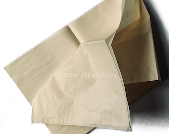 May include: A folded, light brown paper bag, possibly for packaging or crafts, is shown against a white background. The bag has a rectangular shape with visible creases and folds, creating a three-dimensional form. The paper appears thin and slightly translucent.