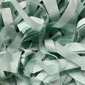 Op de afbeelding: Een stapel lichtgroene tissuepapier-slierten. Het papier is gekreukt en verward, waardoor een textuurrijke achtergrond ontstaat.