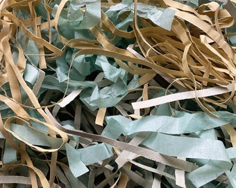 May include: Close-up of shredded paper in shades of tan, light green, and gray. The paper is cut into long, thin strips, creating a textured, layered effect. Ideal for packaging and gift wrapping.