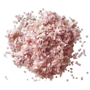 May include: Pink and white confetti made of paper. The confetti is in the shape of small squares and is scattered on a white background.