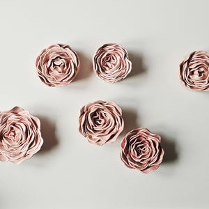 Peut inclure: Sept décorations murales en forme de roses en céramique rose poudré. Les roses sont disposées sur un fond clair. Chaque rose présente de multiples couches de pétales, créant un design floral réaliste. Ces pièces décoratives ajoutent une touche d'élégance.