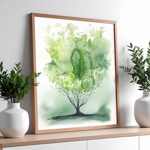 May include: A framed watercolour painting of a tree with a green canopy and a dark trunk. The artwork is displayed on a white surface, with two white vases holding green plants on either side. The frame is light brown.