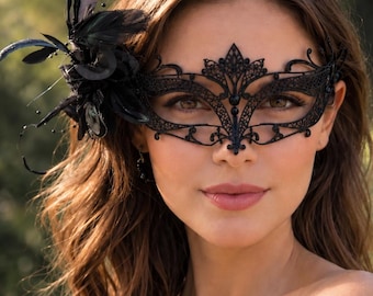 May include: A black lace masquerade mask featuring intricate filigree patterns and a side embellishment of black feathers and thin stems. The mask covers the eye area and includes the text Crystal A. COUTURE in the bottom right corner.