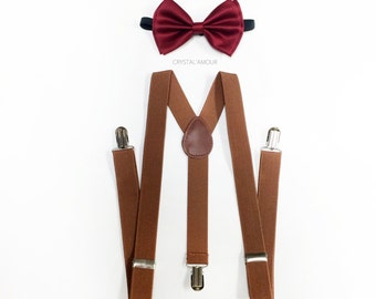 May include: A set of formal wear accessories, including a burgundy bow tie and brown suspenders. The suspenders have silver-colored clips and a leather patch. The bow tie is made of a shiny fabric. The brand name "CRYSTAL'AMOUR" is printed on the image.