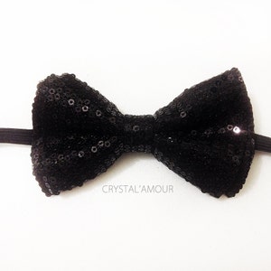 May include: A black bow tie made of sequins. The bow tie is tied with a black elastic band.