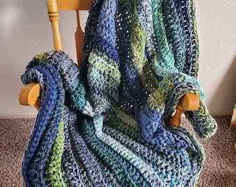 May include: A crocheted blanket in shades of blue, green, and white, draped over a wooden rocking chair.
