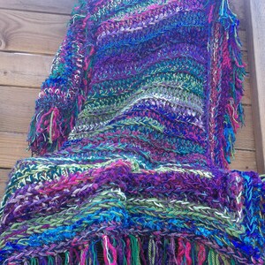 May include: A colorful crocheted shawl with a fringe border. The shawl is made with a variety of colors, including purple, blue, green, and pink.