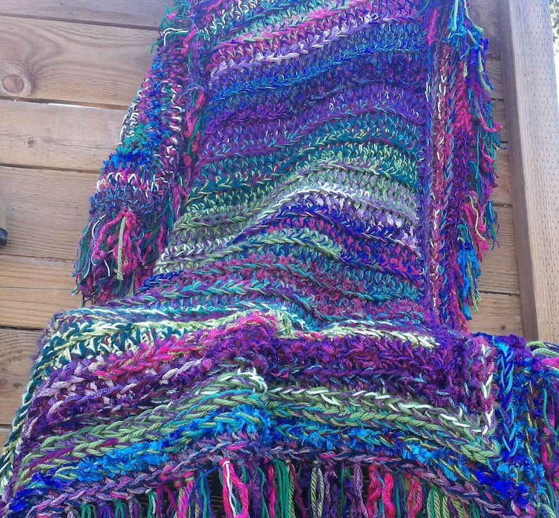 May include: A colorful crocheted shawl with a fringe border. The shawl is made with a variety of colors, including purple, blue, green, and pink.