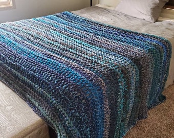 May include: A blue and gray striped crocheted throw blanket on a bed with a gray pillow.