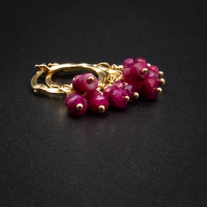 May include: Gold hoop earrings with a cluster of dangling ruby red beads.