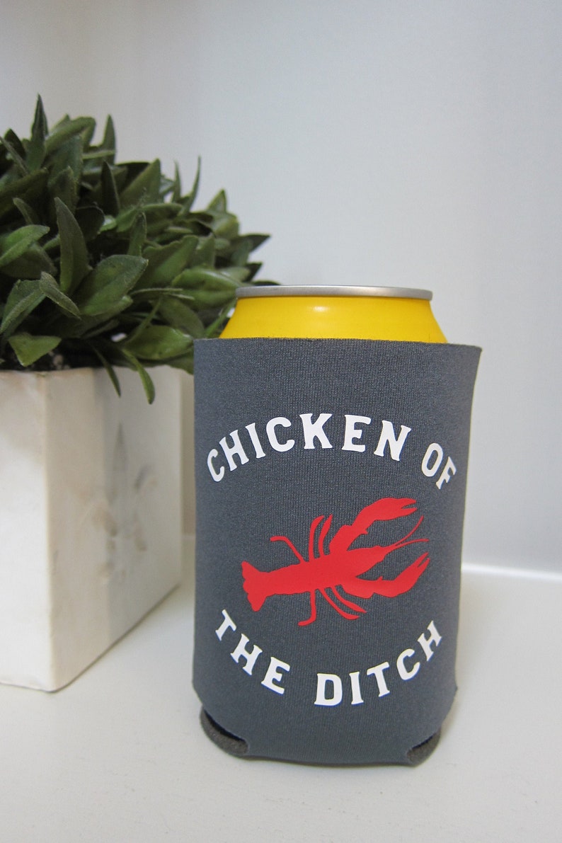May include: Gray can cooler with a yellow top. The cooler has a white graphic that says "Chicken of the Ditch" with a red crawfish illustration.