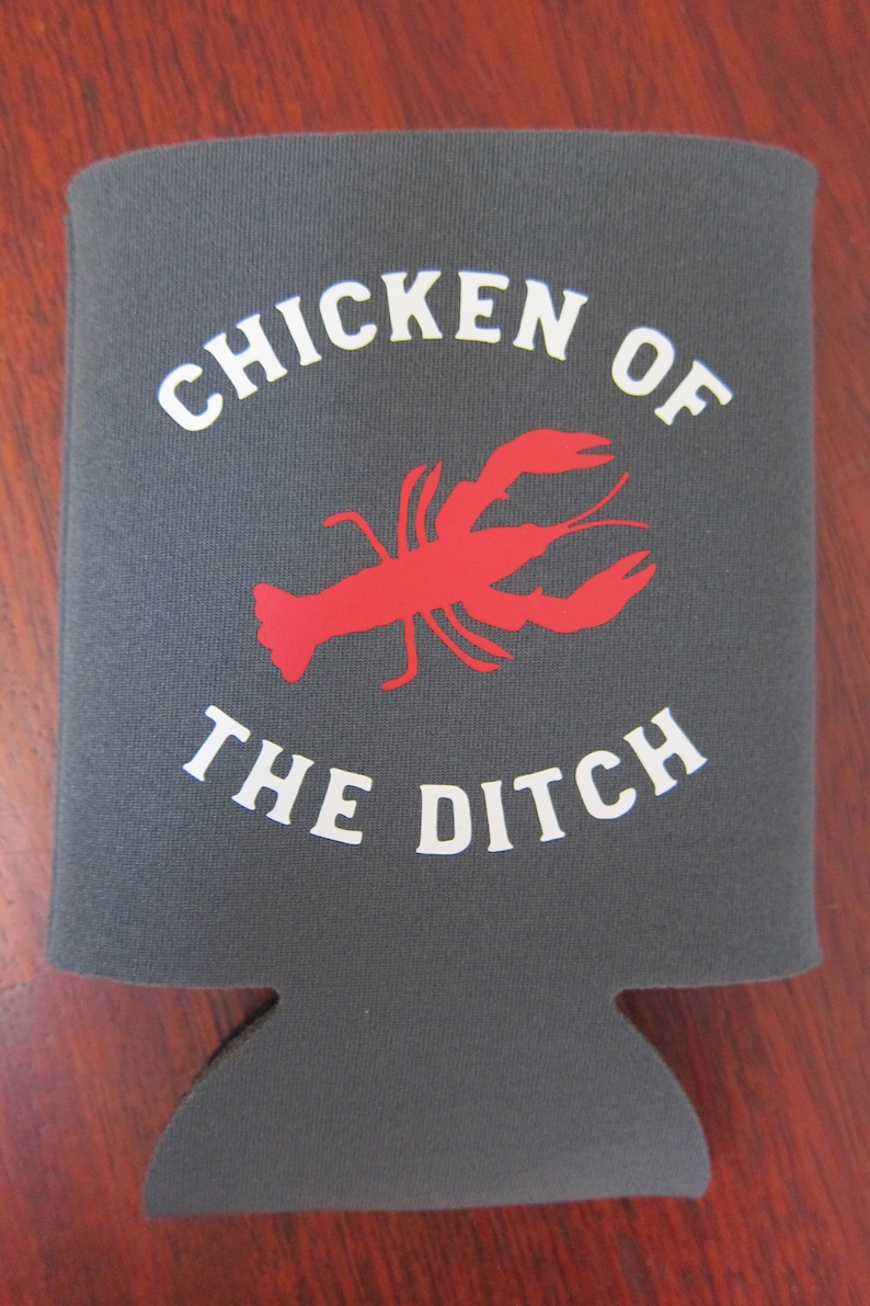 May include: Gray neoprene can cooler with white text that reads "Chicken of the Ditch" and a red silhouette of a crawfish.