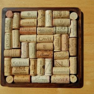 May include: A wooden square frame filled with a grid of used wine corks. The corks have various labels and logos, including "Cavit", "Bogle", "Trellis", "Corbett Canyon", "Primus", "Green Fin", "Atalaya", "White Truck", "Rutherford", "Rioja", "Charles Shaw", "Lorimar", "Sarver", "Newlan", "Ca'Momi", "Sebastiani", "Stephen Ross", "Donataula", "Waterbrook", "Suvereto", "Poppy", "Pouilly-Fume", "Lidei", "Parducci", "Ricard", "US".