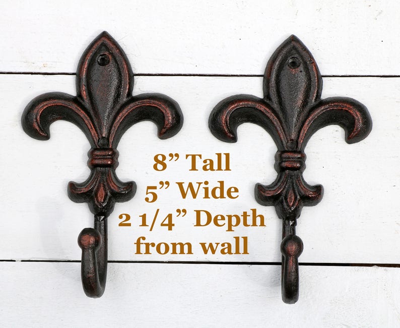 May include: Two black cast iron fleur-de-lis hooks with a brown patina finish. Each hook is 8 inches tall, 5 inches wide, and projects 2 1/4 inches from the wall.